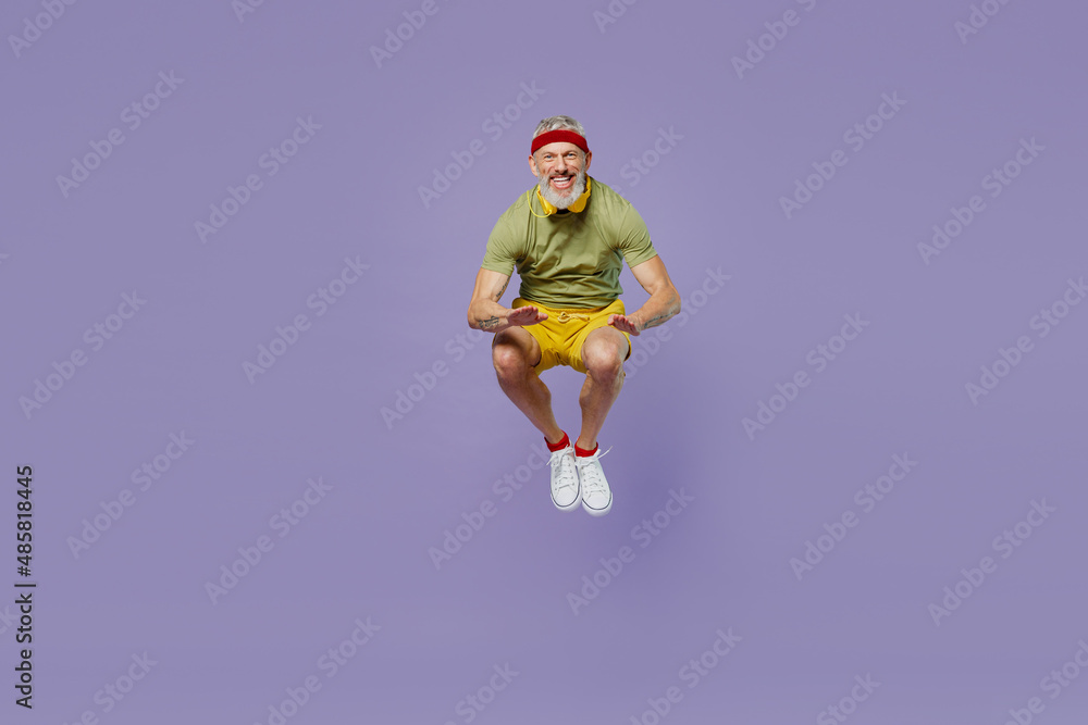 Full size body length vivid sporty elderly gray-haired bearded man 40s years old in headband khaki t-shirt jump touch hands with knees isolated on plain pastel light purple background studio portrait.