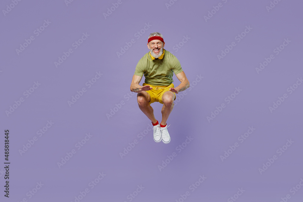 Full size body length vivid sporty elderly gray-haired bearded man 40s years old in headband khaki t-shirt jump touch hands with knees isolated on plain pastel light purple background studio portrait. Full size body length vivid sporty elderly gray-haired bearded man 40s years old in headband khaki t-shirt jump touch hands with knees isolated on plain pastel light purple background studio portrait.