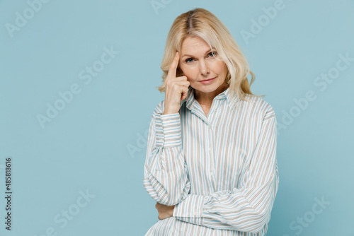 Elderly thoughtful puzzled sad caucasian woman 50s wear striped shirt prop up forehead head look camera isolated on plain pastel light blue color background studio portrait. People lifestyle concept.