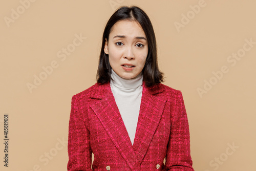 Disappointed displeased sad dissatisfied upset woman of Asian ethnicity wearing red jacket looking camera isolated on plain pastel beige background studio portrait. People lifestyle fashion concept.