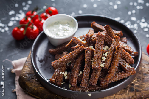 on a wooden cutting kitchen board, homemade food, a plate of black black bread grunch with garlic, an appetizer with sauce, cutlery on a black isolated background, closeup, top photo