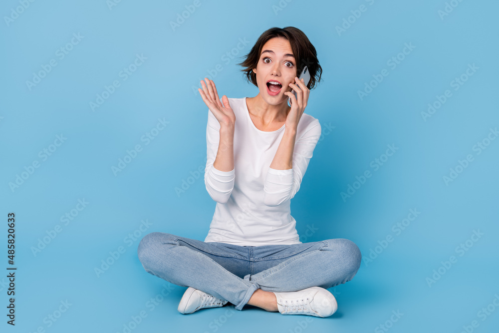 Photo of sweet excited woman wear white shirt legs crossed communicating modern gadget isolated blue color background Photo of sweet excited woman wear white shirt legs crossed communicating modern gadget isolated blue color background