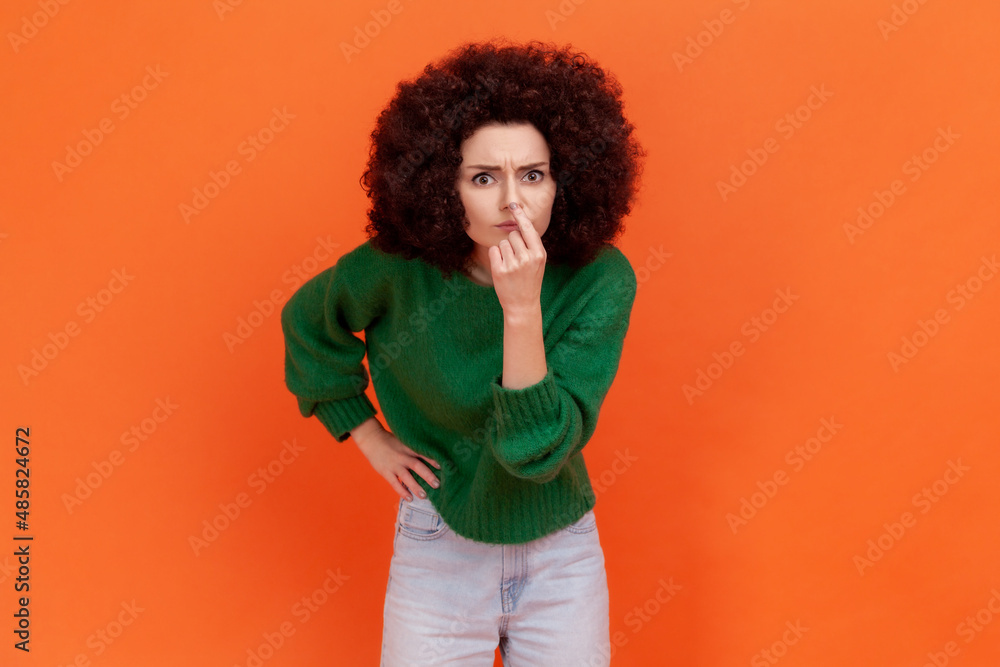 Woman with Afro hairstyle looking with incredulous suspicious gaze and touching nose, gesturing you are liar, suspecting falsehood. Indoor studio shot isolated on orange background. Woman with Afro hairstyle looking with incredulous suspicious gaze and touching nose, gesturing you are liar, suspecting falsehood. Indoor studio shot isolated on orange background.