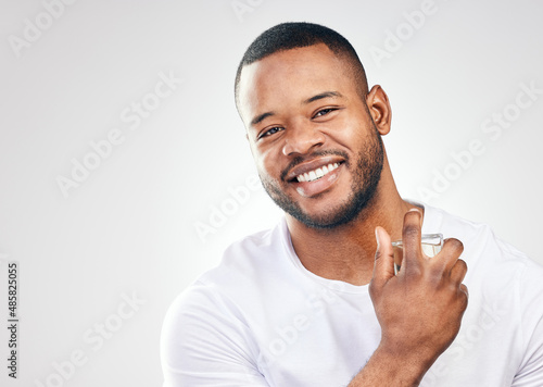 Grooming plays a major role in maintaining a high self-esteem. Studio portrait of a handsome young man spraying perfume on himself against a white background. photo