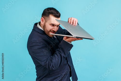 Photography Portrait of curious bearded businessman wearing official style suit carefully peeking into half-opened laptop and spying on forbidden content