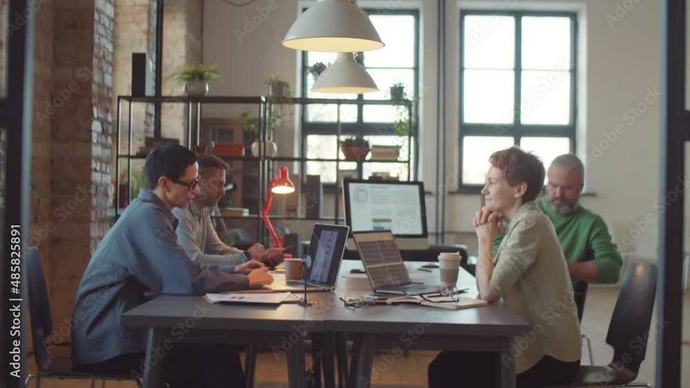 Businesswomen and businessmen using laptops and speaking while working at table in shared office space Businesswomen and businessmen using laptops and speaking while working at table in shared office space