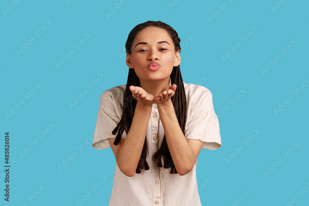 Romantic beautiful woman blowing air kiss, keeps lips folded palm towards mouth, sends mwah coquettish, wants to cheer up her partner. Indoor studio shot isolated on blue background. Romantic beautiful woman blowing air kiss, keeps lips folded palm towards mouth, sends mwah coquettish, wants to cheer up her partner. Indoor studio shot isolated on blue background.