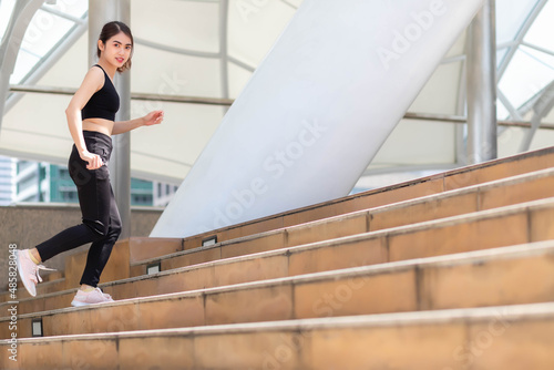 A Southeast Asian woman in gym clothes running up stairs outdoors.