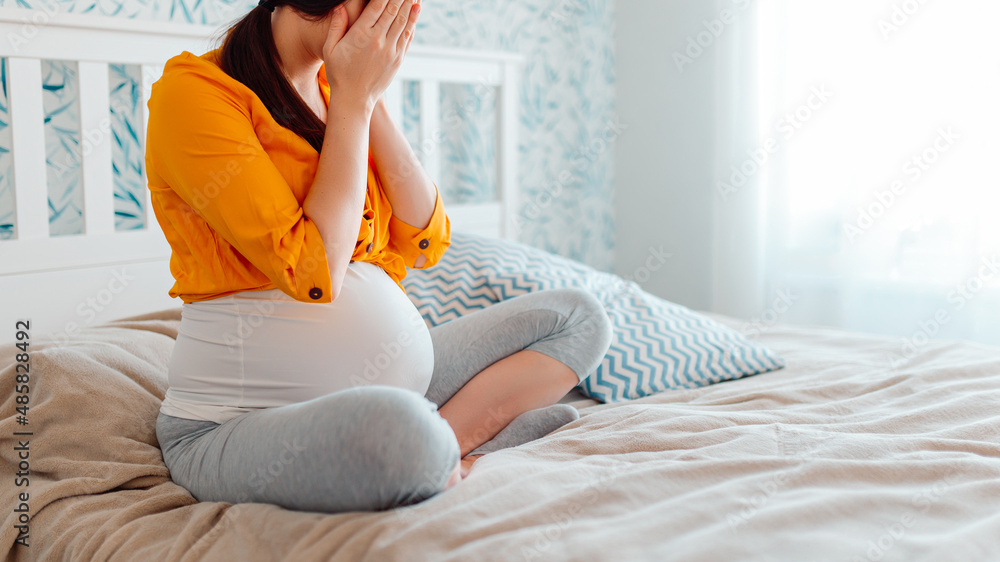 Pregnant woman crying in bed. Pregnant woman closed eyes with hands in bed.