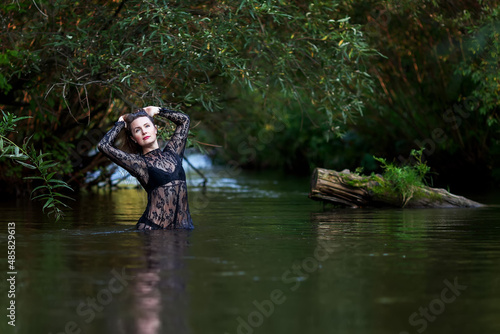 woman in a dark lace dress splashes in the river