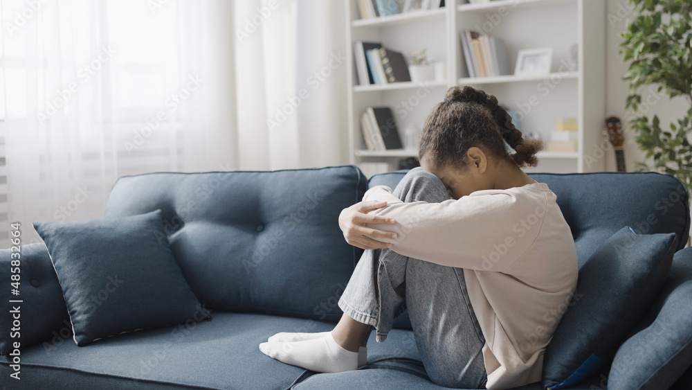 Upset teenage girl sitting on the sofa at home, feeling lonely, family problem Upset teenage girl sitting on the sofa at home, feeling lonely, family problem