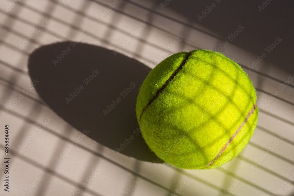 Tennis ball and its shadow on an isolated white background. Tennis ball has shadow of tennis racket net on it.