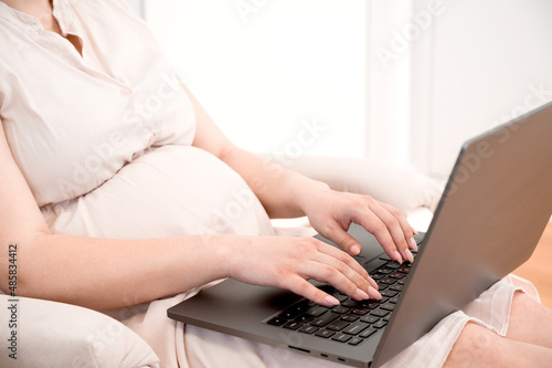 Unrecognizable pregnant woman using laptop for Browsing Internet  Shopping Online Or Reading Maternity Blog. Remote work.Online appointment with a doctor