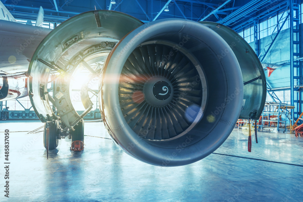 Jet engine with open hood covers on maintenance, illuminated by bright light from behind the hangar gate. Jet engine with open hood covers on maintenance, illuminated by bright light from behind the hangar gate.