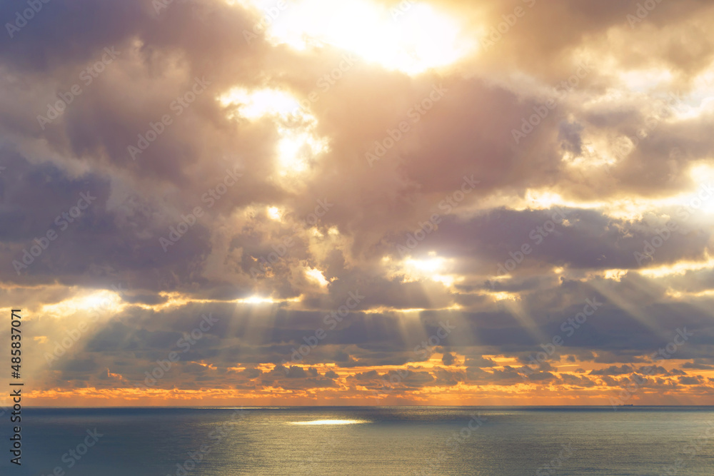 Rays divine holy from the sun behind the clouds break through and illuminate the surface of the sea, before sunset.