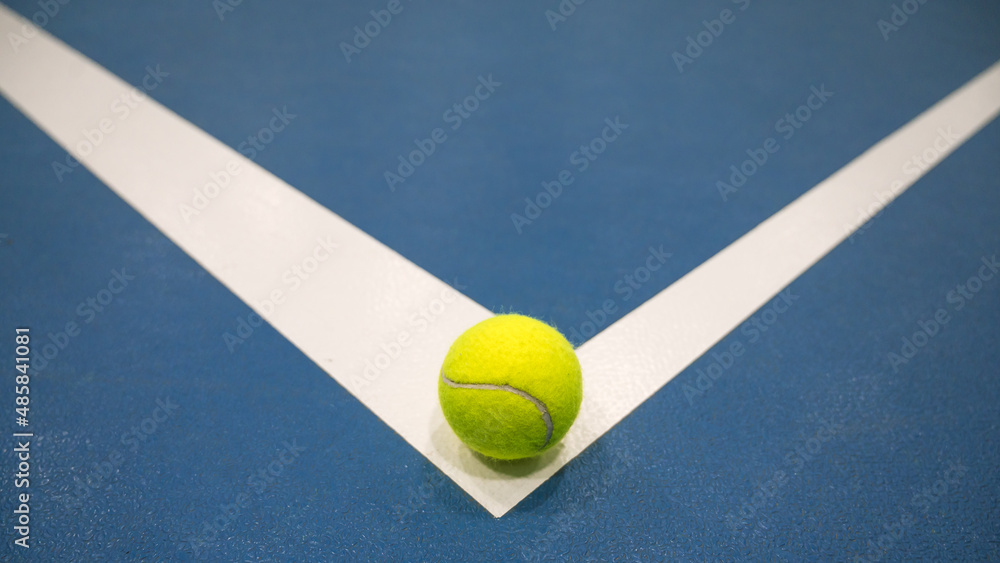 Tennis ball on white line on blue hard tennis court. Close-up.