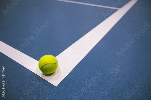 Tennis ball on white line on blue hard tennis court. Close-up. © Anastasia