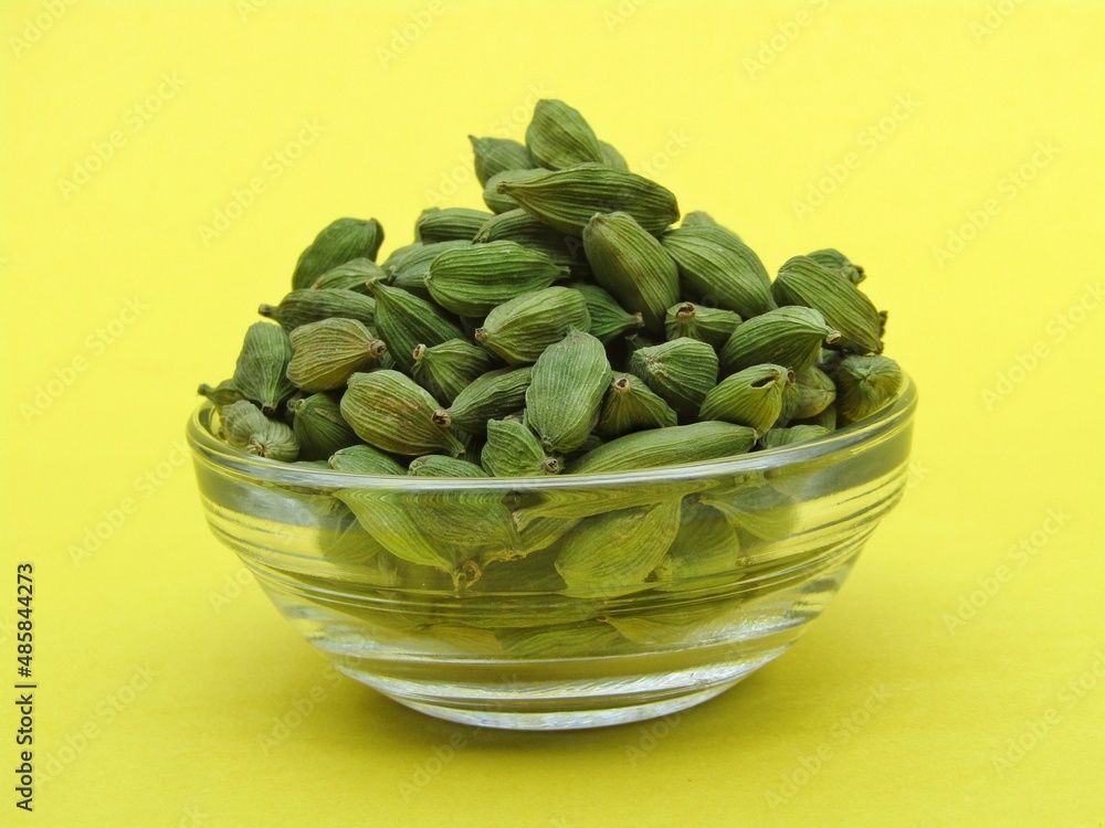 Green Cardamom in a glass bowl on yellow background Green Cardamom in a glass bowl on yellow background