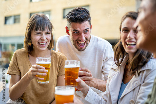 Group of friends drinking beers and laughing, generation z people at pub having fun and toasting with beerglasses, young couples enjoying time together