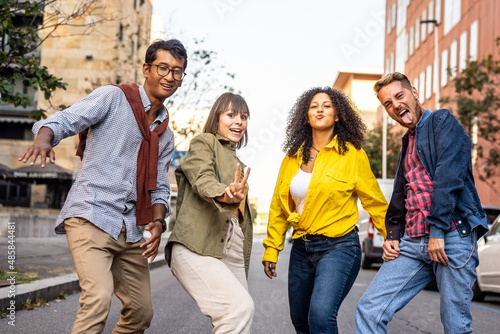 Multiracial group of friends having fun walking in a foolish way by street, party mood, happy university students acting funny moves and steps, smiling young people dancng in the city street
