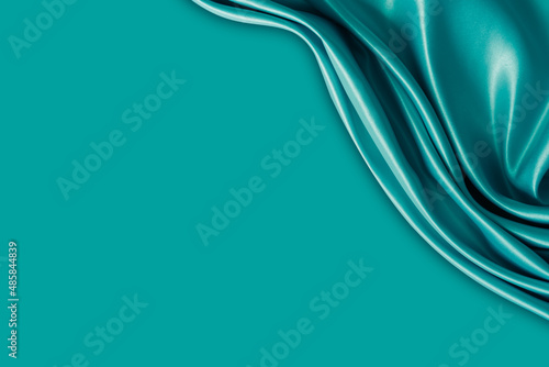 Photography of beautiful wavy turquoise silk satin luxury cloth fabric with monochrome background design. 
