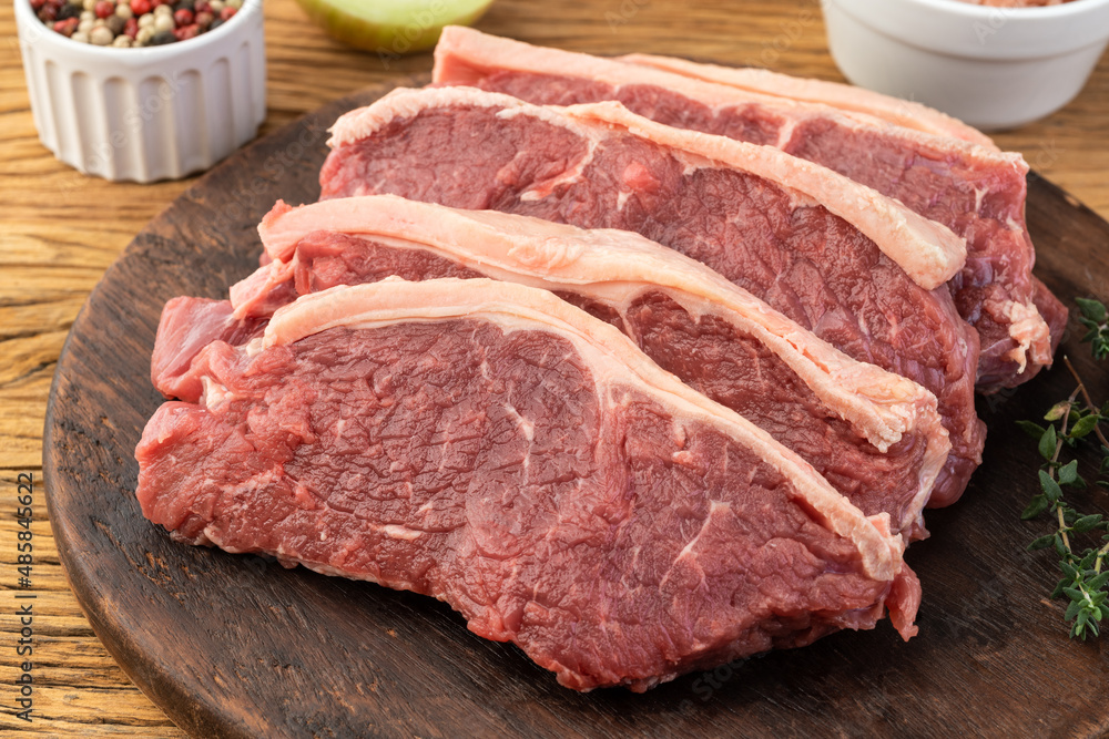 Sliced raw strip loin meat over wooden board with seasonings