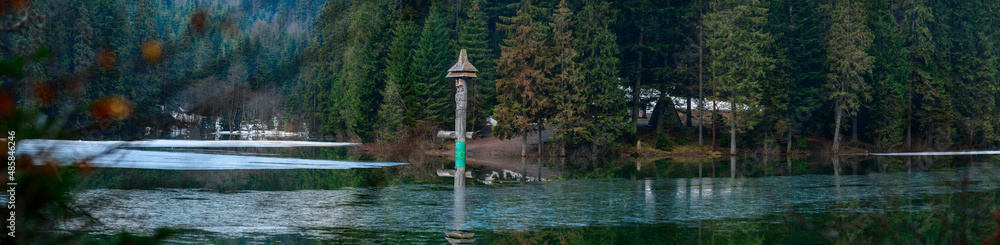 Alpine lake Synevyr, wooden statues near the lake, a tourist place in Ukraine, ice on the lake.