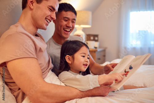 Family With Two Dads In Bed At Home Reading Story To Daughter