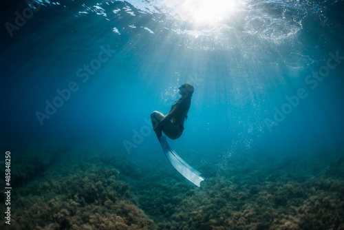 Freediver woman glides with fins in blue ocean. Freediver and beautiful light