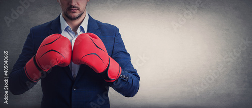 Fényképezés Close up businessman in suit with red boxing gloves stands ready in a fighting stance, punching his fists