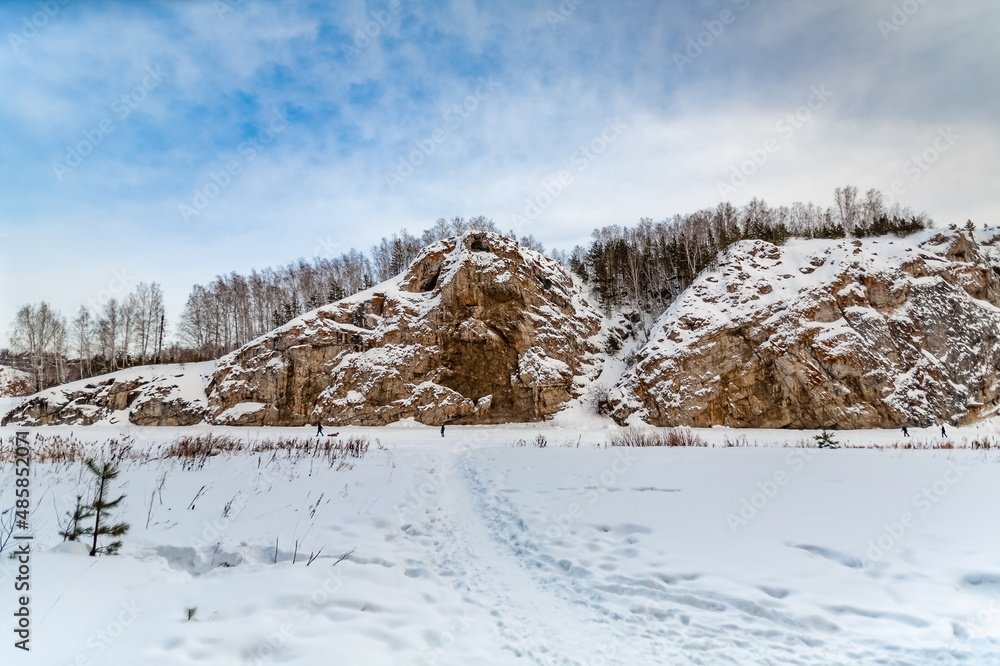 Winter landscape with a big stone, forest, sky from a frozen river