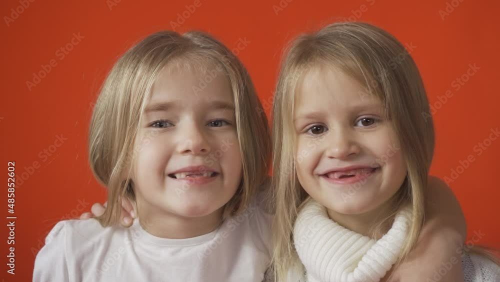 Two little toothless girls are smiling against an orange background. Tooth loss in children. Two little toothless girls are smiling against an orange background. Tooth loss in children.