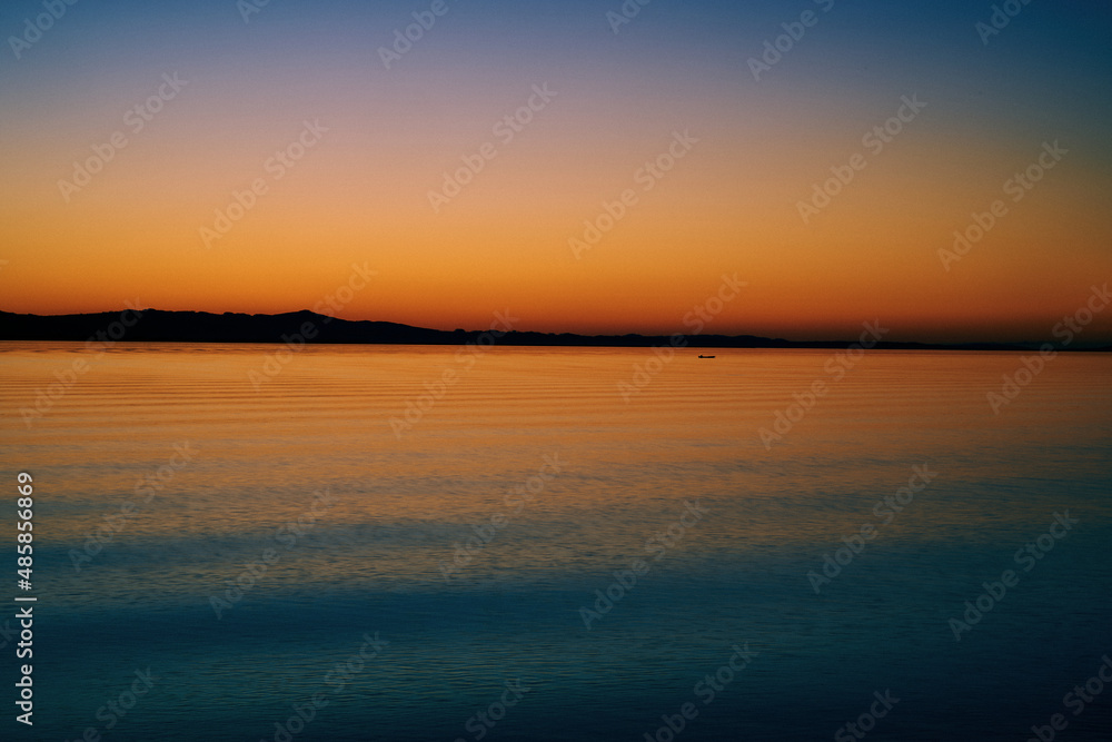 Fototapeta premium A colorful sunset over the sea with the mountains on the horizon