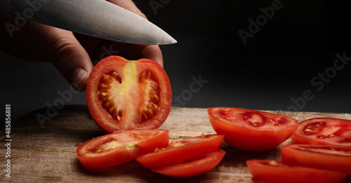 Cherry tomatoes on wooden board cut with knife by female hands on background with copyspace. Healthy organic pomodoro vegetable sliced