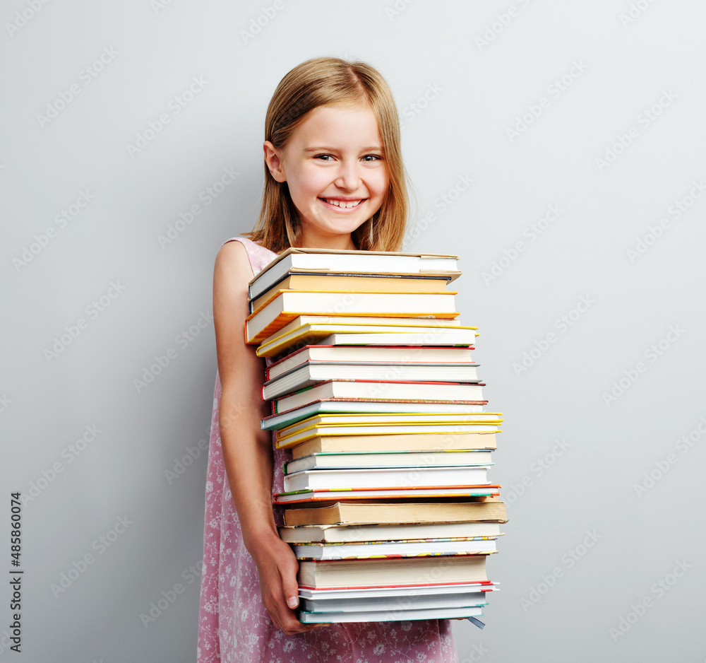 Primary school girl holding stack of books indoors Primary school girl holding stack of books indoors