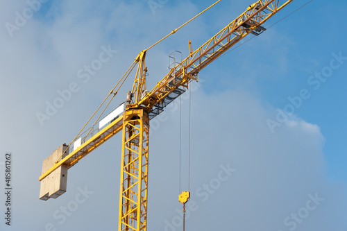 A lonely yellow tower crane on the sky background