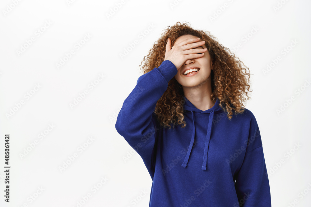 Happy young woman close eyes and smiles, waits for surprise, stands over white background in casual clothes Happy young woman close eyes and smiles, waits for surprise, stands over white background in casual clothes
