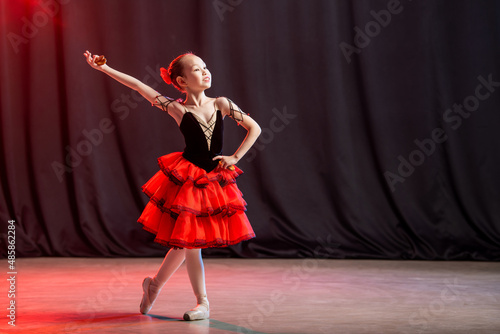 A little girl ballerina is dancing on stage in a tutu on pointe shoes with castanedas, the classic variation of Kitri.