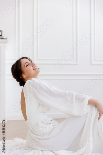 A woman in a white airy dress sits on the floor, smiling and laughing. Emotion and joy, blurred in motion image.
