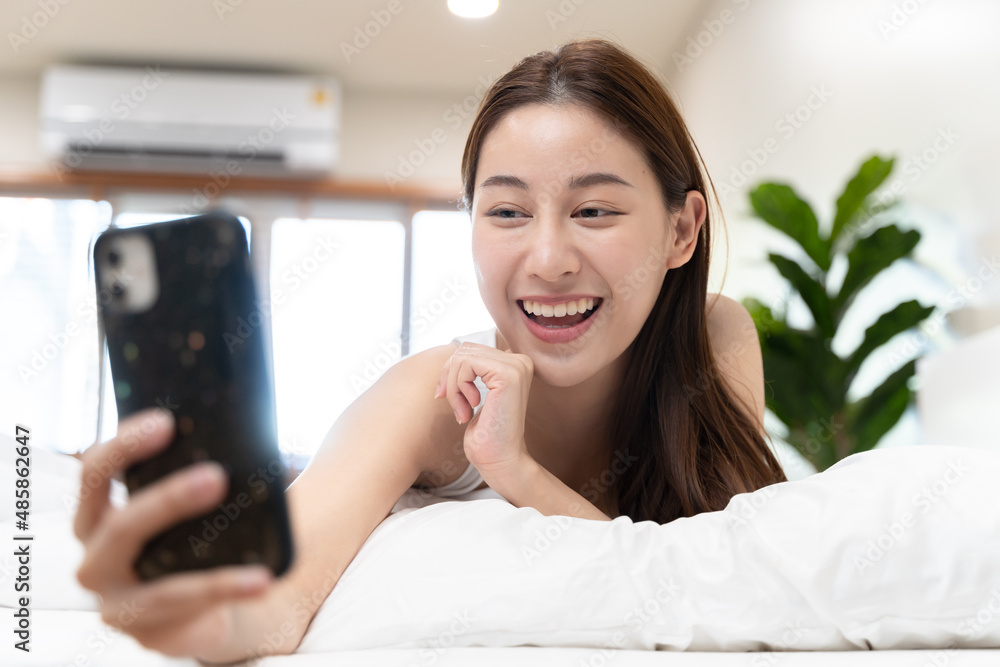 Happy Asian woman conference call via smartphone with her friends on the bed at home Happy Asian woman conference call via smartphone with her friends on the bed at home