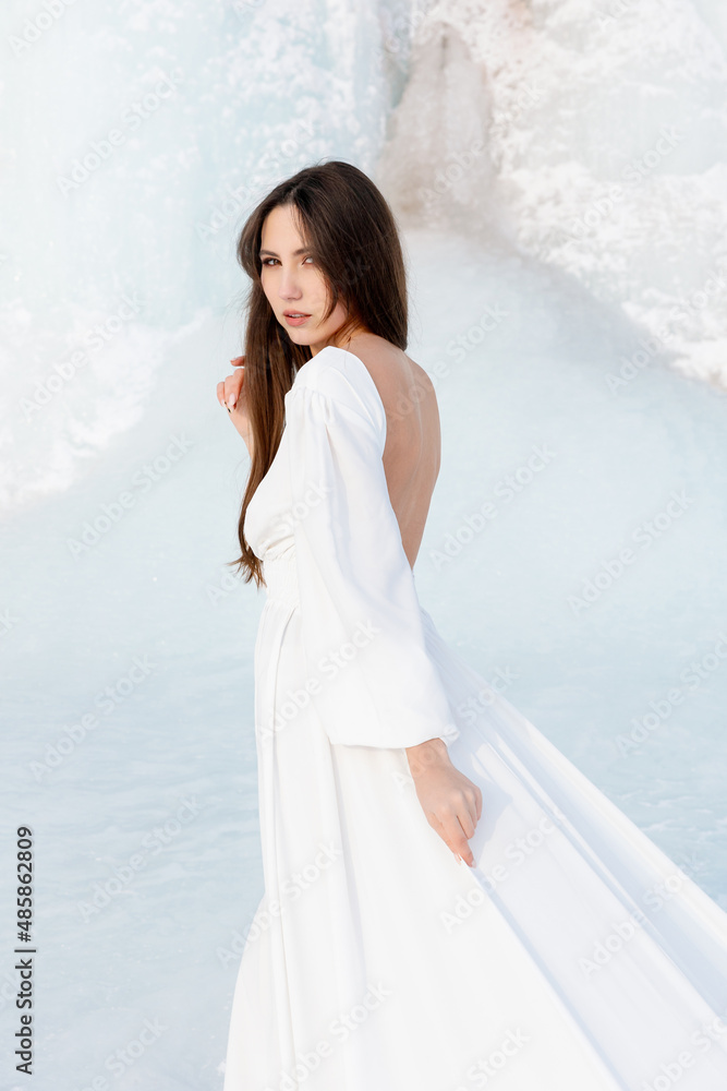 Portrait of a beautiful young woman, she poses in a white flying dress against a backdrop of a frozen coast covered in blue ice. Fancy dress Portrait of a beautiful young woman, she poses in a white flying dress against a backdrop of a frozen coast covered in blue ice. Fancy dress