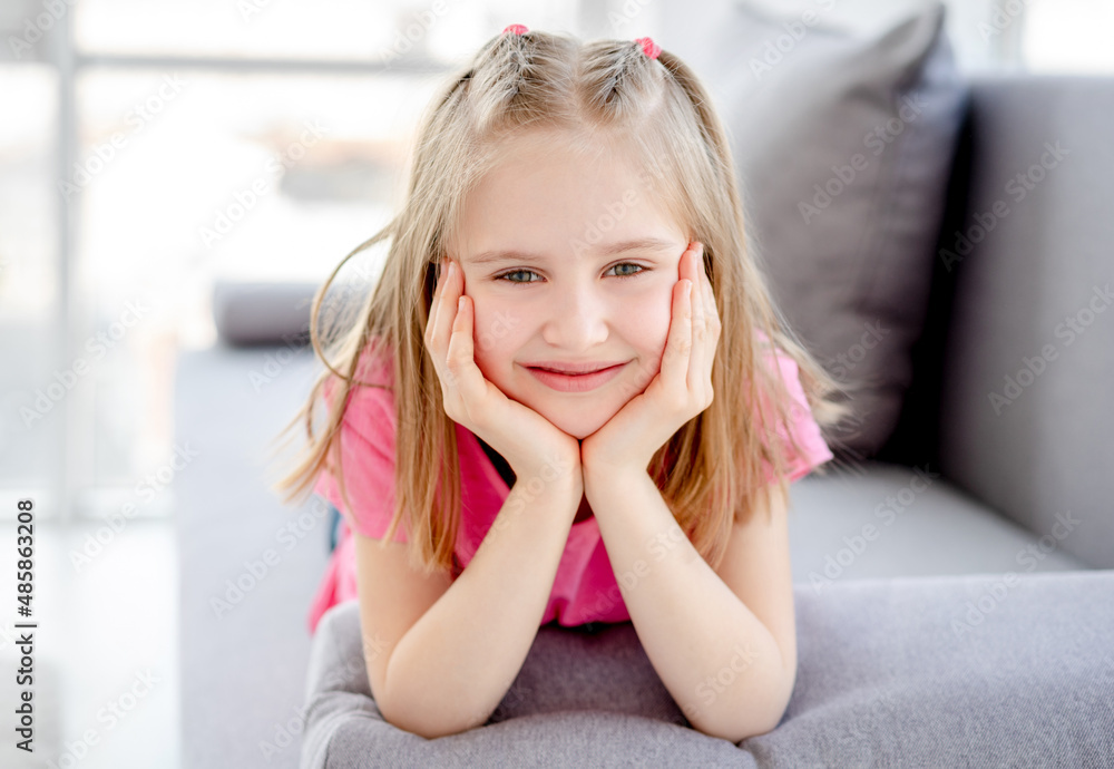 Happy little girl resting on sofa with head on hands indoors Happy little girl resting on sofa with head on hands indoors
