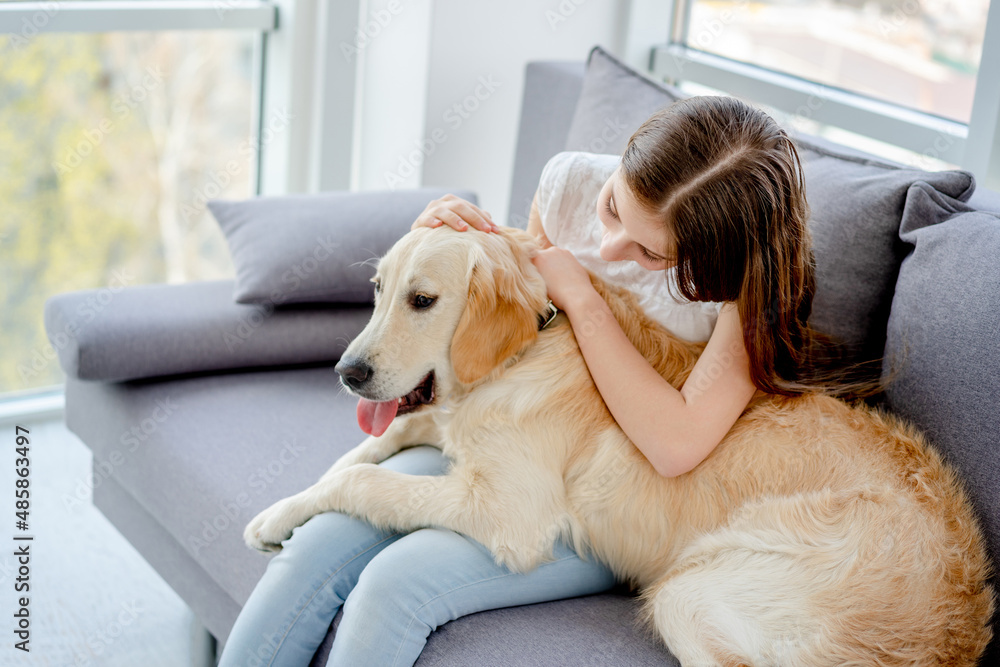 Sweet girl holding cute dog sitting on sofa indoors Sweet girl holding cute dog sitting on sofa indoors