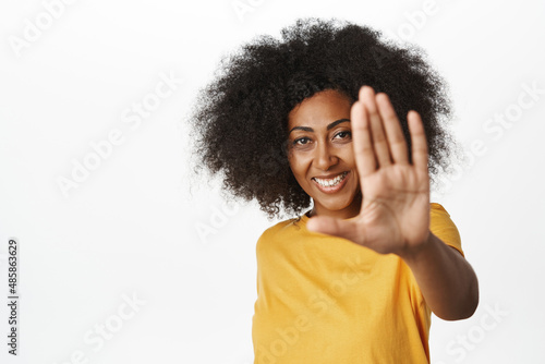 Portrait of smiling african american woman extends hand  shows palm  number five  looking happy at camera  standing over white background