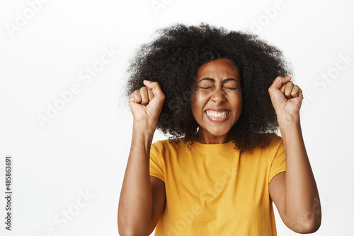 Enthusiastic Black woman winning and celebrating, triumphing, smiling pleased, achieve goal, standing over white background