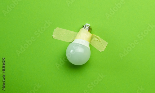 Lamp lightbulb attached with tape on green background. Concept of creativity and invention