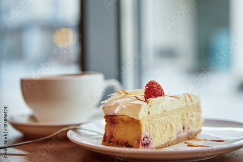 Cup of coffee and piece of raspberry cheesecake on cafe table near window  breakfast at public place