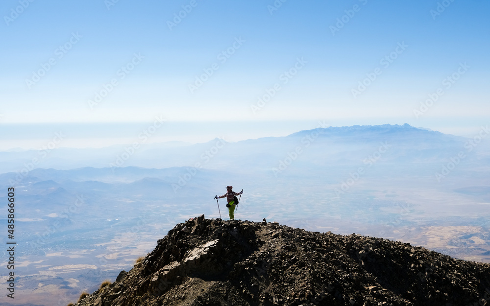 Tourist standing on volcanic mountain top with raised hands