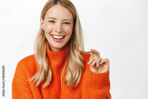 Beautiful woman with blond natural hair, no makeup and clean glowing face, white smile, posing in red winter sweater, looking at camera sensual, standing over white background