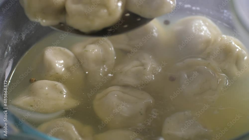 Boiled dumplings with meat are taken out of boiling water with an iron colander. Transparent glassware. Close-up. Boiled dumplings with meat are taken out of boiling water with an iron colander. Transparent glassware. Close-up.